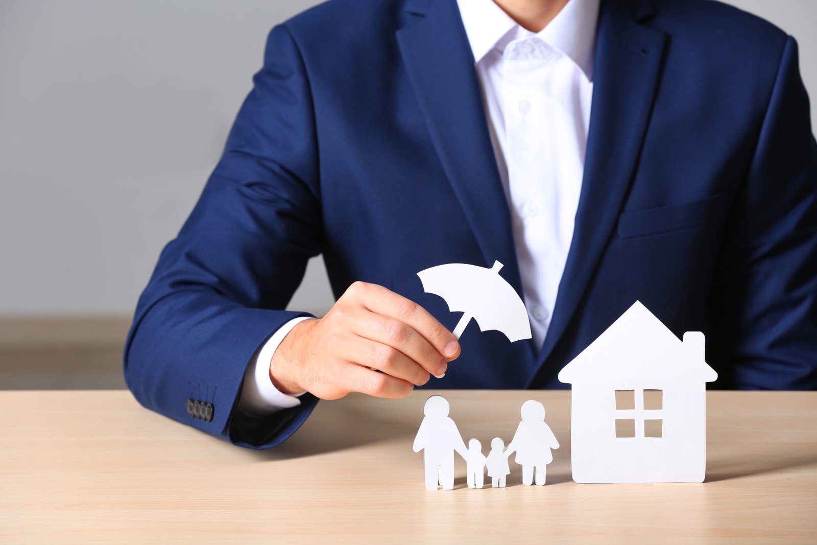 Male insurance agent covering paper family and home with umbrella cutout at table, closeup Male insurance agent covering paper family and home with umbrella cutout at table, closeup